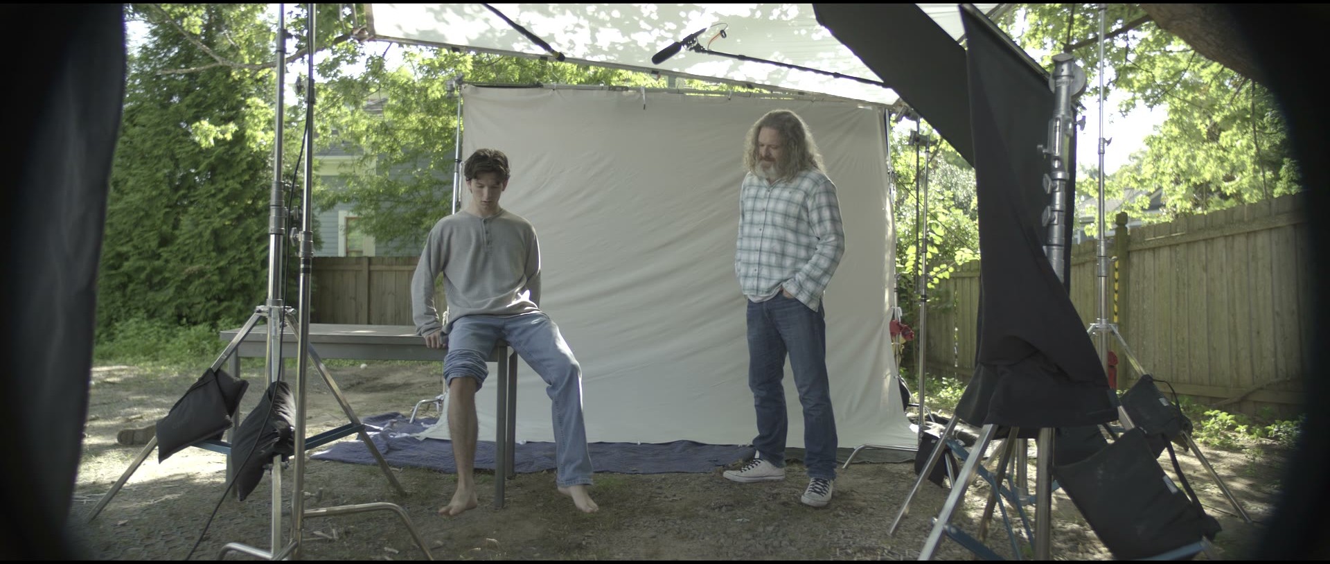 Camera original: the actor seated on a table and Bob standing in front of a white sheet in a backyard, film gear around them